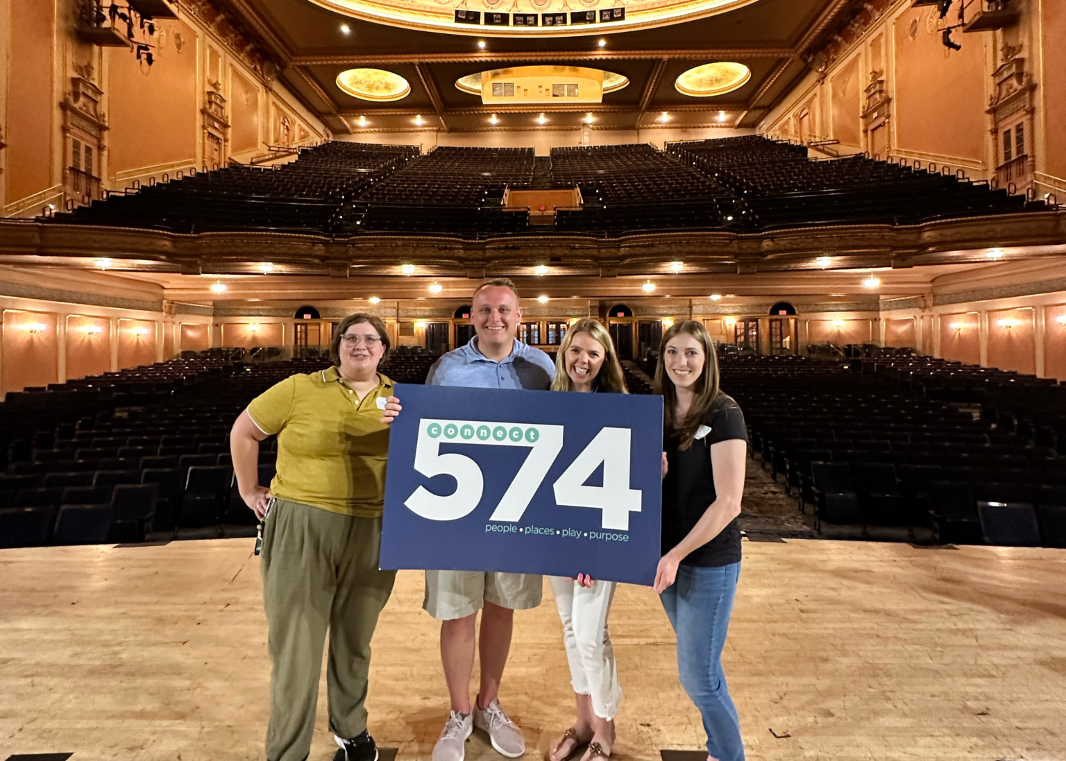 Four Connect 574 members holding the logo sign on stage at the Morris Performing Arts Center